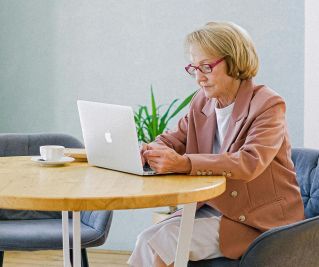 Elderly woman with glasses using a laptop at a bright, modern home interior.