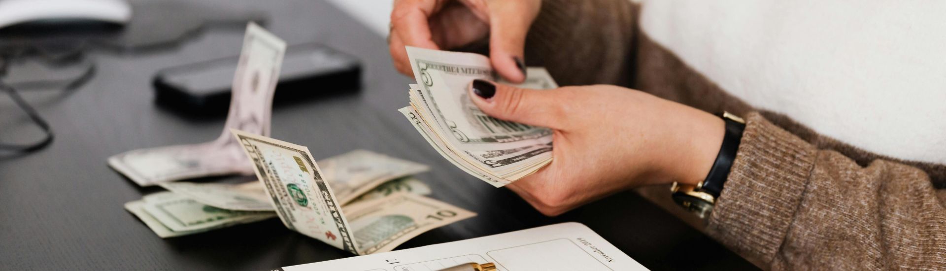 Close-up of person counting cash with notepad on desk, indicating financial tasks.